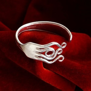Può includere: Un braccialetto d'argento realizzato con una forchetta riutilizzata. I rebbi della forchetta sono stati piegati in un design decorativo a spirale. Il braccialetto è esposto su uno sfondo di velluto rosso.