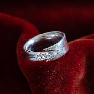 Könnte beinhalten: Ein silberner Ring mit einem floralen Design, auf einem roten Samt Hintergrund.