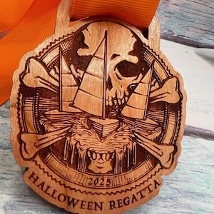 May include: A circular wooden medal featuring a laser-engraved design of a skull, crossbones, and a sailboat on water. The text "HALLOWEEN REGATTA" and "2025" are engraved at the bottom. The medal is attached to a bright orange ribbon.
