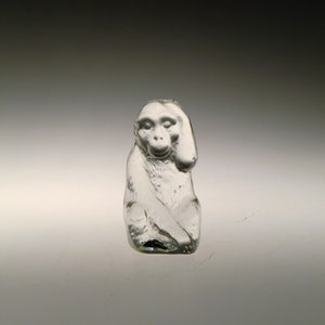 May include: A clear glass figurine of a monkey sitting with its head tilted to the side.