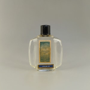 May include: A clear glass bottle of Floramix Jasmin perfume with a black cap. The bottle has a gold label with the text "Floramix" and "Jasmin" in blue.