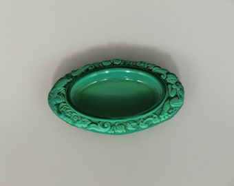 May include: A green oval-shaped dish with a decorative, raised, floral design around the rim.
