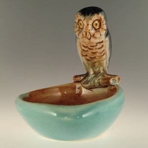 Peut inclure: Une figurine d'hibou en céramique perchée sur une branche, avec un bol bleu sarcelle en dessous. Le hibou a des marques brunes et noires et des yeux jaunes.