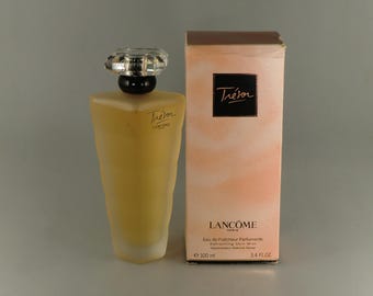 Puede incluir: Un frasco de perfume Lancôme Trésor con un tapón transparente facetado y un frasco de vidrio esmerilado teñido de amarillo. La caja es de color melocotón con el logotipo de Trésor e información del producto. Contiene 100 ml de bruma refrescante para la piel.