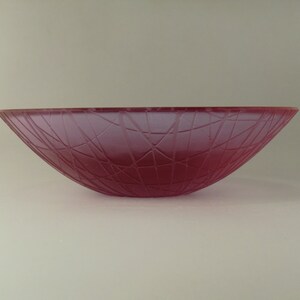 May include: A deep pink glass bowl with a textured, geometric pattern. The bowl is slightly curved and has a wide opening.