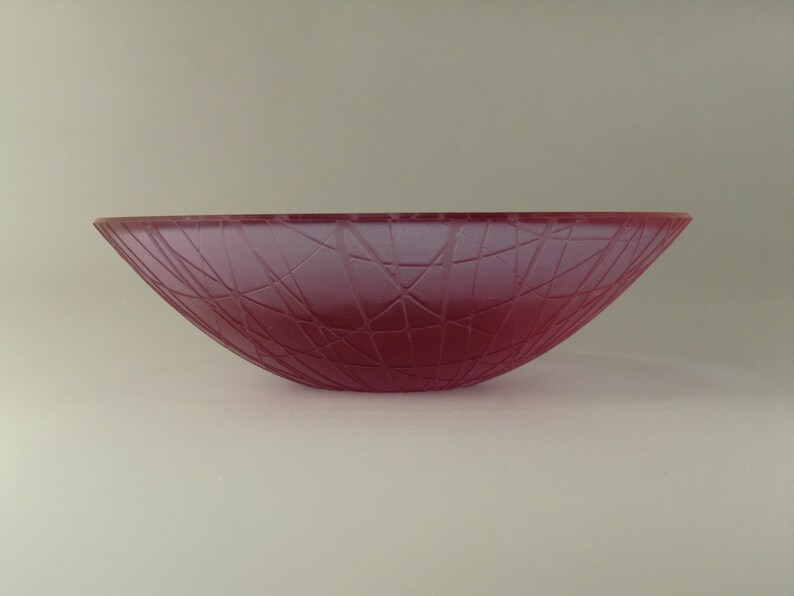 May include: A deep pink glass bowl with a textured, geometric pattern. The bowl is slightly curved and has a wide opening.