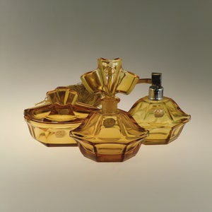 Pode incluir: Um conjunto de três frascos de perfume de vidro âmbar com rolhas ornamentadas. Os frascos têm um design facetado e são decorados com etiquetas douradas.