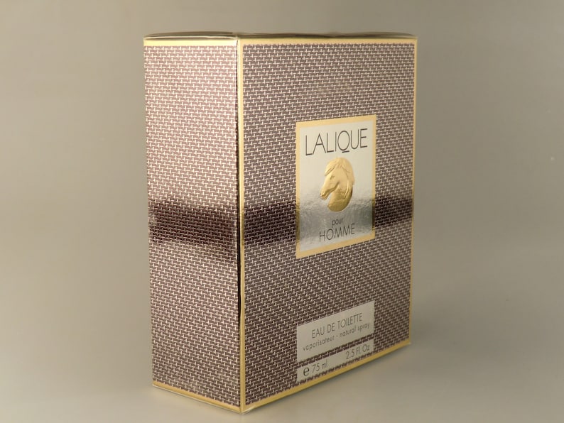 K&ouml;nnte beinhalten: Eine braune und goldene Schachtel mit einem goldenen Pferdelogo und dem Text "Lalique pour Homme" auf der Vorderseite. Die Schachtel ist mit "Eau de Toilette vaporisateur - nat&uuml;rlicher Spr&uuml;hkopf e 75 ml 2.5 fl. oz." beschriftet.
