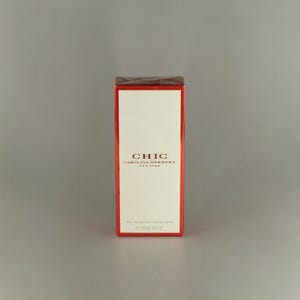 May include: A red-bordered perfume box with a white central panel. The word "CHIC" is displayed prominently, with "CAROLINA HERRERA NEW YORK" beneath. The box contains 50 ml of perfume, equivalent to approximately 1.7 fluid ounces.