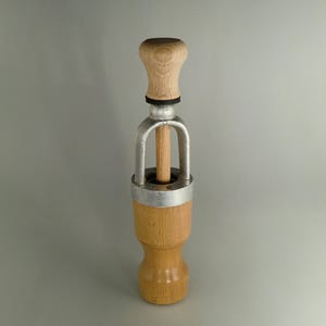 Peut inclure: Un bouchon de bouteille en bois et en métal avec un bouton en bois sur le dessus. Le bouchon est conçu pour s'adapter au goulot d'une bouteille et possède un anneau métallique autour du milieu.