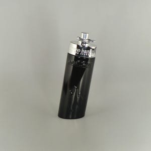 May include: A black perfume bottle with a silver cap. The bottle is inscribed with "bruno banani" and "man". The bottle has a curved shape and a silver top.