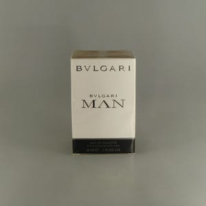 May include: A white rectangular box of Bvlgari Man Eau de Toilette. The box features the brand name "BVLGARI" and the product name "MAN" in black text. The bottom of the box reads "30 ml 1 FL OZ US".