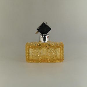May include: A clear glass bottle with a textured surface and a silver atomizer. The bottle is filled with a yellow liquid.