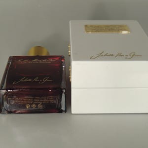 Op de afbeelding: Een donkerrode glazen fles parfum met een gouden dop en een witte doos. De fles heeft de tekst "Juliette Has a Gun" erop. De doos heeft de tekst "Juliette Has a Gun" erop.