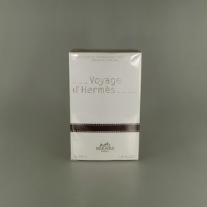 May include: A white rectangular box of "Voyage d'Hermès" eau de toilette. The box has a brown band across the middle and the Hermes logo at the bottom. The text on the box includes "35 ml" and "1.18 fl oz."