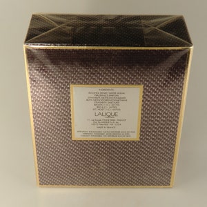 K&ouml;nnte beinhalten: Eine braune Schachtel mit goldenen Verzierungen und einem wei&szlig;en Etikett, auf dem die Inhaltsstoffe des Lalique-Parf&uuml;ms aufgef&uuml;hrt sind. Das Etikett enth&auml;lt den Text "Lalique Perfume" und "Made in France".