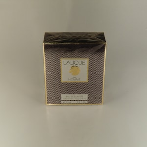 K&ouml;nnte beinhalten: Eine braune und goldene Schachtel mit dem Text "Lalique Pour Homme" und "Eau de Toilette Natural Spray" darauf. Die Schachtel ist 75 ml oder 2,5 fl oz.
