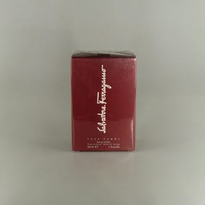May include: A burgundy box of Salvatore Ferragamo Pour Homme Eau de Toilette. The box displays the brand name in white script and product details. The bottle contains 30 ml of product.