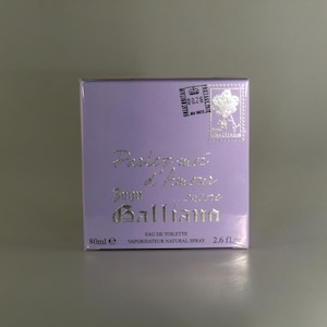 May include: A lavender-coloured perfume box with silver lettering. The box reads "Parlez-moi d'Amour" and "John Galliano". It contains 80ml of Eau de Toilette and 2.6 fl oz. A stamp is visible on the top right corner.
