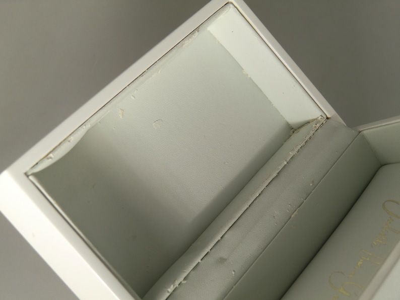 Op de afbeelding: Witte juwelendoos met een wit fluwelen interieur. De doos is open en het deksel is opengeklapt.