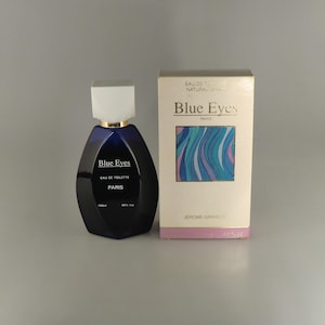 May include: A dark blue perfume bottle with a white cap and gold trim, next to a matching box. The box features the text "Blue Eyes Paris" and a colorful wave design. The bottle contains 100ml of perfume.