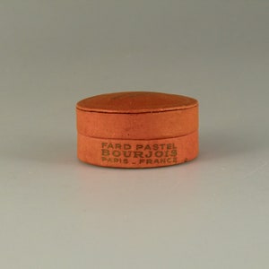 May include: A round, orange cardboard box with the text "FARD PASTEL BOURJOIS PARIS - FRANCE" printed on the side.