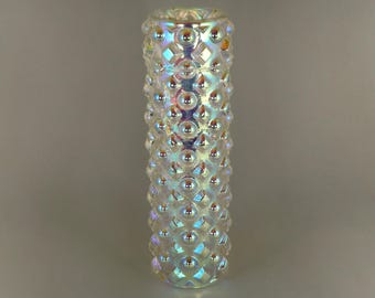 May include: Iridescent glass vase with a cylindrical shape. The vase is covered in a pattern of raised, rounded bumps. The glass reflects a rainbow of colors, including blue, green, and yellow. The vase is approximately 6 inches tall.
