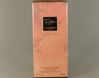 Puede incluir: Una botella rosa y blanca de bruma hidratante para el cuerpo Lancôme Trésor. La botella está etiquetada con "Eau de soin précieuse pour le corps" y "Fragranced body moisture mist". La botella es de 6,7 fl oz (200 ml).