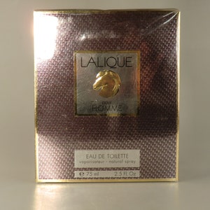 K&ouml;nnte beinhalten: Eine goldene und braune Schachtel mit einem goldenen Etikett, auf dem "LALIQUE pour HOMME" und ein goldenes Pferdekopflogo stehen. Die Schachtel ist f&uuml;r ein 75 ml Flakon Eau de Toilette.