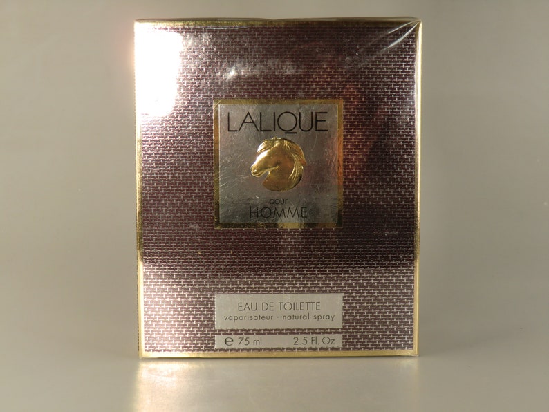 K&ouml;nnte beinhalten: Eine goldene und braune Schachtel mit einem goldenen Etikett, auf dem "LALIQUE pour HOMME" und ein goldenes Pferdekopflogo stehen. Die Schachtel ist f&uuml;r ein 75 ml Flakon Eau de Toilette.