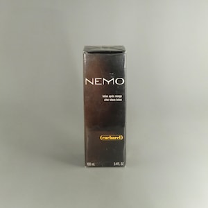 May include: A rectangular box of Cacharel Nemo aftershave lotion. The box is dark brown with the word "NEMO" in white at the top. The text "lotion après rasage after shave lotion" is below the word "NEMO". The box contains 100 ml (3.4 fl oz).