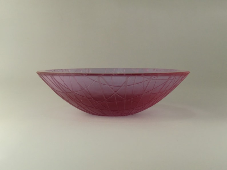 May include: A pink glass bowl with a textured, geometric design. The bowl is slightly curved and has a wide, shallow opening.
