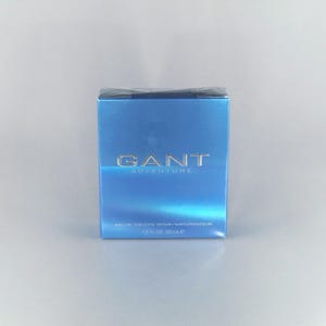 May include: A light blue box of GANT Adventure Eau de Toilette Spray. The box has silver lettering and the text "1.7 fl oz 50ml". The box is sealed in clear plastic.