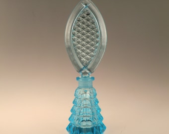Può includere: Un flacone di profumo in vetro blu con un design testurizzato a forma di diamante. Il flacone ha una base conica a più livelli e un tappo appuntito a forma di foglia.