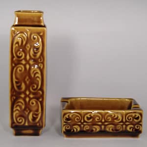 Op de afbeelding: Een set van twee bruine keramische vazen met een decoratief swirl-patroon. De langere vaas is rechthoekig en de kortere vaas is een vierkante asbak.