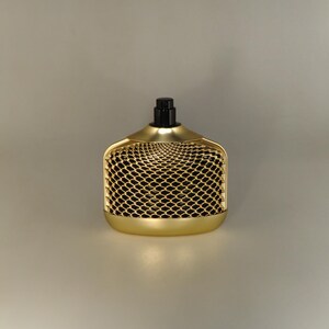 May include: A gold-coloured bottle with a black cap and a mesh design. The bottle is sitting on a white surface.