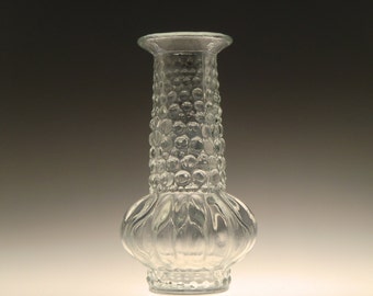 May include: A clear glass vase with a textured, bubble-like design. The vase has a round, bulbous base and a narrow neck.