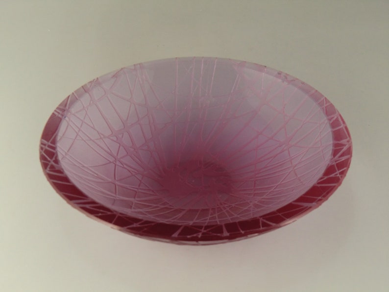 May include: A pink glass bowl with a frosted finish and a spiderweb design.