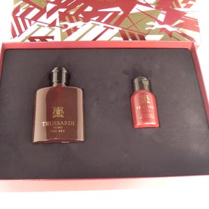 May include: A Trussardi Uomo The Red gift set, comprising a large and small red bottle. The bottles have black caps and are presented in a red box with a patterned lid. The set is designed for fragrance.