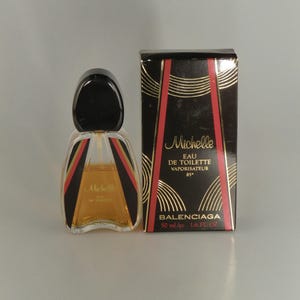 May include: A vintage "Michelle" Eau de Toilette perfume bottle and box by Balenciaga. The bottle has a black cap and a geometric design with red and black accents. The box is black with gold and red details.