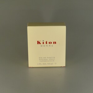 May include: An off-white rectangular box of Kiton Donna Eau de Parfum. The brand name is in red, with the text "Eau de Parfum Natural Spray Vaporisateur" below. The box contains 1 fl. oz. / 50 ml.