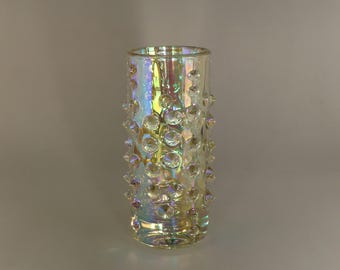May include: A clear glass vase with a textured, iridescent surface. The vase has a cylindrical shape and is decorated with small, raised bumps.