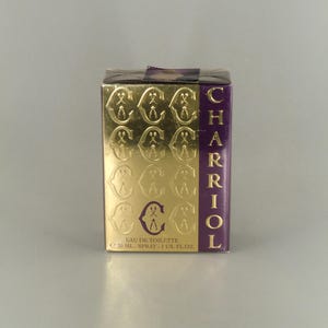 May include: A rectangular perfume box with gold embossed repeating "C" and "A" symbols on a gold background. The right side of the box is purple with the word "CHARIOL" in gold lettering. The box contains 30 ml of Eau de Toilette.