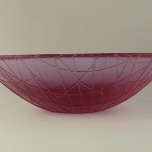 May include: A deep pink glass bowl with a geometric pattern. The bowl is frosted and has a wide, shallow shape.