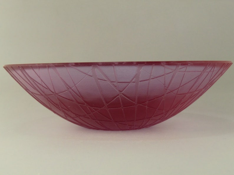 May include: A deep pink glass bowl with a geometric pattern. The bowl is frosted and has a wide, shallow shape.