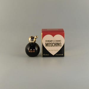May include: A small bottle of Cheap and Chic Moschino Eau de Toilette in a black and gold bottle with a red and gold box. The box has a heart with the brand name on it. The bottle is 0.16 US fl oz.