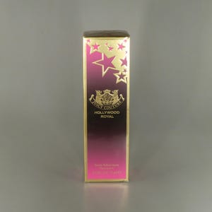 May include: A gold and pink bottle of Juicy Couture Hollywood Royal Eau de Parfum spray. The bottle is decorated with gold stars and the Juicy Couture logo.