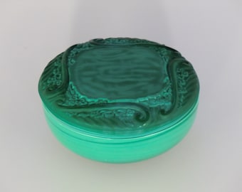 May include: A green glass trinket box with an ornate design on the lid. The box is round and has a smooth, glossy finish.