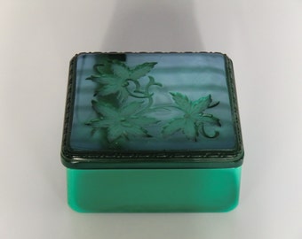May include: A square green glass trinket box with a raised floral design on the lid. The lid is a darker shade of green than the box.