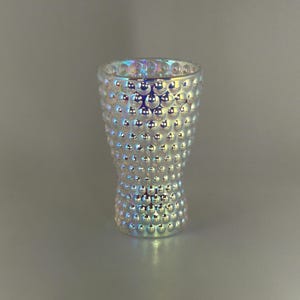 Peut inclure: Un vase en verre transparent et irisé avec un motif texturé en forme de bulles. Le vase a un dessus évasé et une base plus étroite en forme de sablier. Le verre reflète un arc-en-ciel de couleurs.
